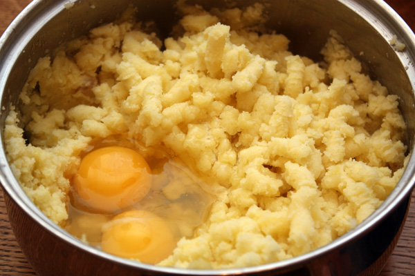 Пока картошка не остыла, разомните ее вместе с маслом так, чтобы получилась масса без комочков. Теперь сюда нужно добавить яйца, примерно полторы столовых ложки муки и тщательно перемешать до однородности.