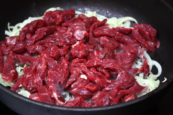 К луку добавить мясо, посыпанное солью и перцем, жарить на сильном огне 5-6 минут, помешивая.
