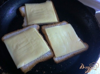 На другой сковороде поджариваем без масла тостовый хлеб с одной строны, переворачиваем и кладем  на обжаренную сторону пластинку сыра. Накрываем крышкой и даем сыр рсплавится.