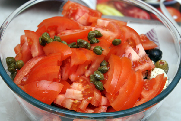 Теперь в ход идет главный компонент греческого салата — помидоры. Их надо 4 штуки, они должны быть спелыми и упругими.  Кроме того, добавим немного каперсов.  Осталось добавить соли, оливкового масла и хорошо перемешать.  Приятного аппетита!