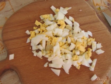 Чистим яйца, нарезаем мелкими кусочками и отправляем в кастрюлю, вслед за огурцами и колбасой.
