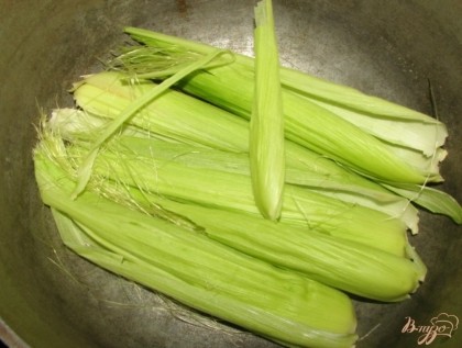 Очищаем кукурузу от листвы и волосков. Берем глубокую кастрюлю, я лично предпочитаю готовить кукурузу в чугунке, выкладываем на дно толстым слоем кукурузную листву.