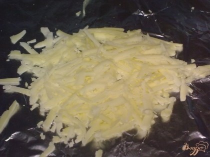 Твердый сыр натрите на крупной терке. Половину выложите на фольгу.