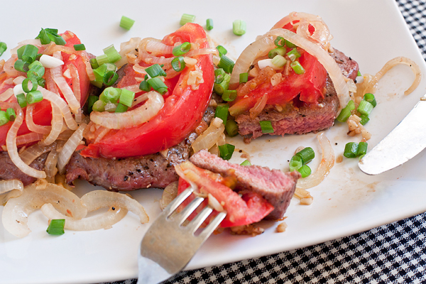 Выложите овощи поверх мяса, посыпьте нарезанной зеленью и подавайте, пока блюдо горячее.