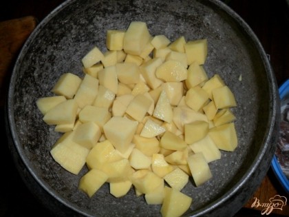 Картофель почистить, нарезать небольшими кубиками, половину сложить в чугунок или кастрюлю с толстым дном.
