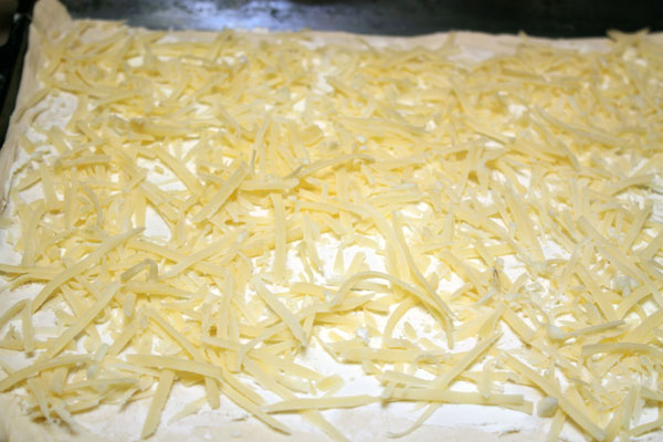 Половину всего теста раскатываем довольно тонко. Распределяем по поверхности теста сливочный сыр и посыпаем крупно натертым пармезаном.