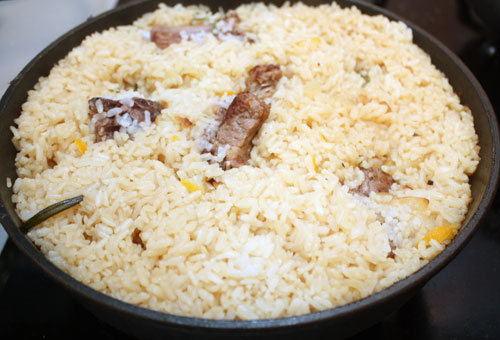 Рис высыпаем в сковороду с мясом, добавляем соль. Аккуратно перемешиваем, для того, чтобы рис покрылся маслом. Через 5 минут добавляем в сковороду кипяток так, чтобы он слегка покрыл рис, убавляем огонь, накрываем крышкой и готовим около 20 минут, пока вода не впитается. 