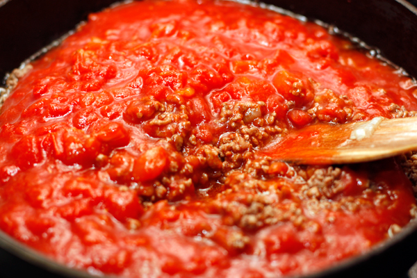 Когда фарш будет готов, в него нужно добавить измельченные помидоры без кожицы. Это может быть готовое томатное пюре (пассата), измельченные томаты в собственном соку, или свежие помидоры, очищенные от кожицы и мелко нарезанные.  Продолжайте готовить на небольшом огне минут 10, чтобы лишняя жидкость испарилась. В конце добавьте зелень.  