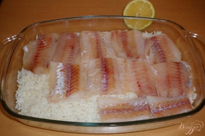 В форму для запекания выложить рис, сверху - сбрызнутое лимонным соком рыбное филе.