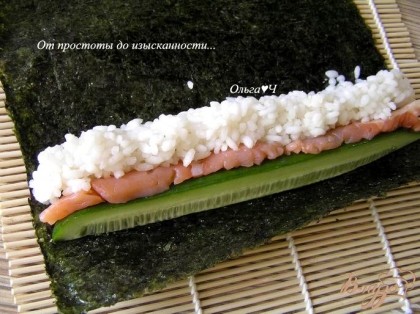 Лист нори положить на специальный бамбуковый коврик для суши. На лист нори выложить огурец, рядом положить полоску лосося и рис.
