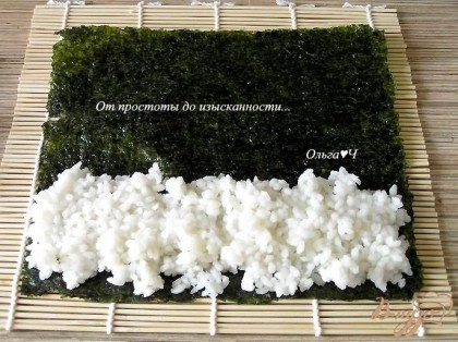 На специальный бамбуковый коврик положить лист нори, сверху выложить горсть риса на 1/4-1/3 листа,