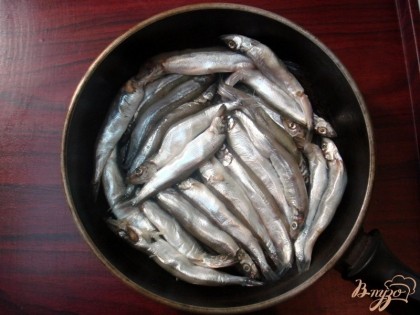 На дно глубокой сковороды выкладываем плотно друг к другу половину рыбки. посыпаем половиной лаврового листа и душистого перца.
