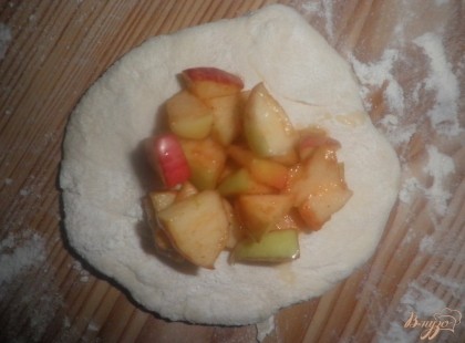 Достать тесто и поделить на 20 равных кусочков, каждый из которых раскатать в лепешку, положить на нее ложку яблок