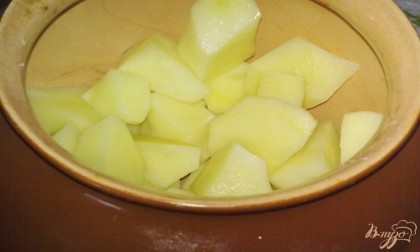 Картофель очистите, вымойте и нарежьте кубиками. На дно горшочка положите кусочек сливочного масла, а затем выложите кубики картофеля.