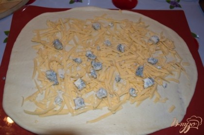 Натрите на терку твердый сыр. Нарежьте сыр Дор Блу. Разложите сыр по поверхности теста. Тут же добавьте нарезанный чеснок и зелень.
