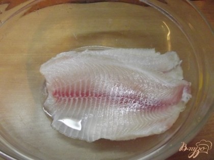 Филе пангасиуса или другой не жирной рыбы разморозьте и положите в глубокую миску. Смешайте лимонный сок пополам с водой и залейте этой смесью рыбу. Оставьте на 10-15 минут.