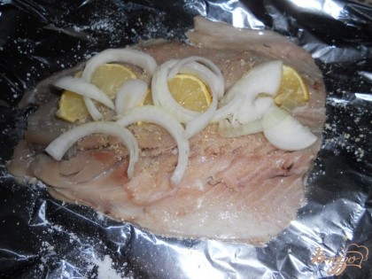На одну половину рыбы выкладываю дольки лимона и полукольца лука.