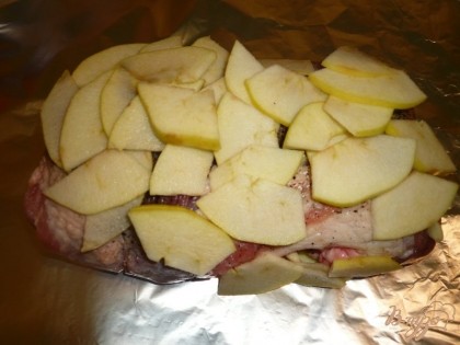 Для приготовления свинины с яблоками используем фольгу или рукав (пакет) для запекания. Расстилаем на столе два куска фольги крест-накрест, по центру фольги выкладываем мясо. Сверху на свинину плотным слоем выкладываем нарезанные яблоки.