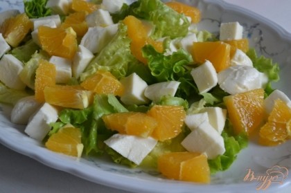 На тарелку выложить листья салата, кусочки апельсина и сыра.
