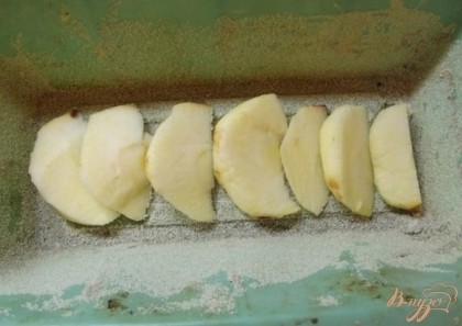 Одно яблоко нарежьте дольками толщиной примерно в сантиметр и уложите дольки на дно формы так, как это показано на фото. Форму при этом предварительно смажьте сливочным маслом и посыпьте манной крупой.