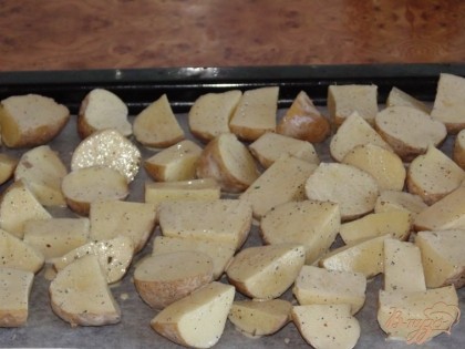 Противень застилаем специальной бумагой для выпечки.  Или же можно просто смазать оливковым или подсолнечным маслом. Выкладываем картофель. Выкладывать нужно кожурой вниз. Сверху можно полить оставшимся соусом. Ставим в заранее разогретую до 180-190 градусов духовку. И выпекаем около 30-40 минут.  Время выпечки зависит от размера кусочков, на которые мы нарезали картофель. Готовность картофеля можно проверить зубочисткой, она должна мягко входить.