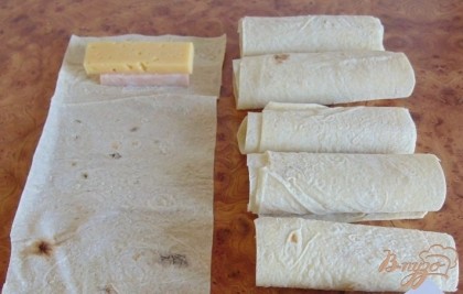 В верхнюю часть полос лаваша выкладываем друг на друга сыр с ветчиной и сворачиваем до конца лаваша. Получились маленькие рулетики.
