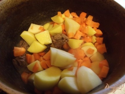 По прошествии 40 минут добавьте к мясу картофель и морковь. Добавьте воды, чтобы она покрывала все на половину. Посолите, добавьте травы, перемешайте. Тушите под крышкой 10-15 минут до мягкости картофеля.