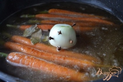 Добавить бульон, луковицу с гвоздикой, лавровый лист и соль по вкусу.Сковороду накрыть крышкой и оставить вариться до полной готовности моркови, на тихом огне.