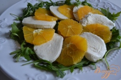 На тарелку выложить листики руколлы и уложить кружочки апельсина и сыра.