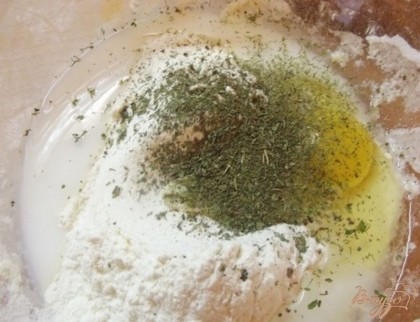 В отдельной посуде смешиваем муку, желток и травы. Дальше добавляем в тесто соль 1 ч. л. и щепотку сахара. Дальше вливаем молоко. Молоко можно влить все сразу. Теперь замешиваем крутое тесто.