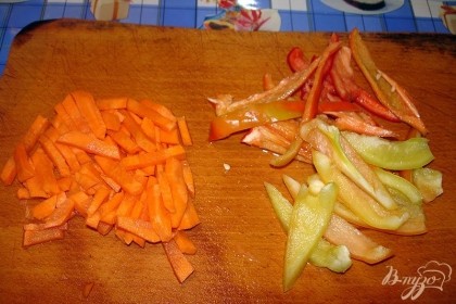 Большую антипригарную сковороду разогреть. Влить немного растительного масла. Болгарский перец нарезать полукольцами. Морковь нарезать крупной соломкой.