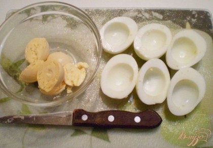 Куриные яйца порежьте на половинки, достаньте желтки, отложите в сторону, они понадобятся для заправки салата.