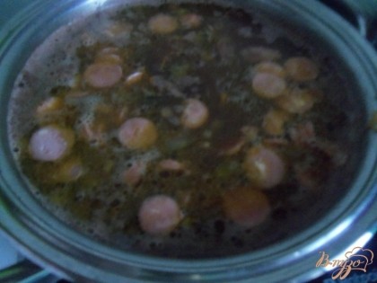 В готовый суп добавить спассерованные овощи, сосиски и варить ещё 5 минут.