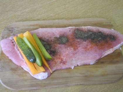 Посыпать свинину специями, на край мяса положить огурец и морковь