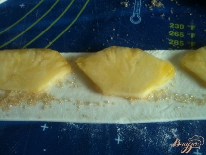 Тесто разрезать на широкие полоски, посыпать сахаром и разложить ломтики ананаса.