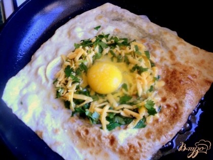 Перевернуть лаваш, по центру выложить натертый сыр с зеленью, сделать углубление и вбить в него яйцо.