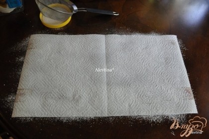 Подготовим бумажное полотенце или кухонное чистое, постелив его на стол под размер противня с бисквитом. Посыпаем сах.пудру ситечком на полотенце.
