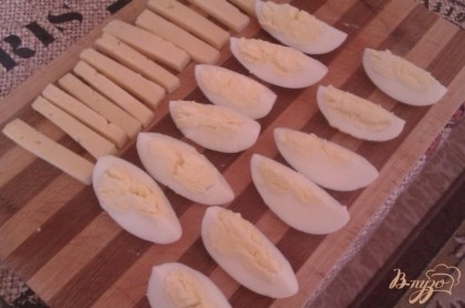 Отварные яйца освобождаем от скорлупы и нарезаем их на четыре продольные дольки. Сыр режем брусочками.