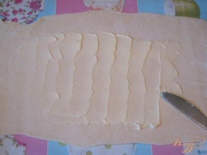 Пласт слоеного теста раскатать в прямоугольник, который смазать сливочным или плавленым сыром.