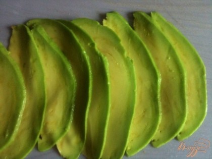 Авокадо разрезать на две части, вынуть косточку и снять кожицу. Нарезать тонко.На рабочий стол разложить кусок пищевой пленки и выложить тонкие ломтики авокадо.