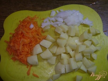Тем временем трем морковку на большой терке, мелкими кубиками режем оставшуюся половину луковицы, картошку чистим и режем небольшими кубиками.
