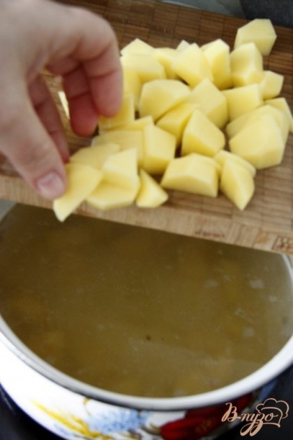 Добавить в кипящий бульон картофель, нарезанный кубиками.