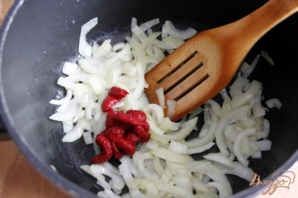 В большой кастрюле разогреть растительное масло, обжарить лук до прозрачности, добавить томатную пасту.