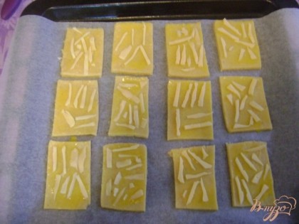 Отделяем желток от белка, и желтком смазываем каждое печенье, режем тонко ножом оставшийся сыр и в произвольной форме выкладываем на печенье.