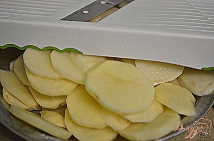 Нарезать картофель помытый и очищенный тонко,используя слайсер или ножом.