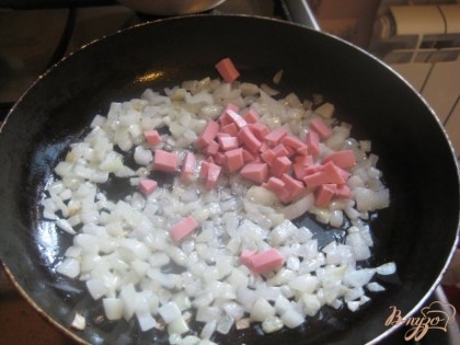 Когда лук чуть зазолотится, добавить нарезанную такими же кубиками колбасу. Перемешать, продолжать обжаривать.