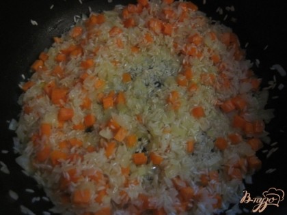 Жарить овощи до прозрачности лука. Выложить в сковороду рис, хорошо перемешать и дать ему "насытиться" маслом и овощами. Налить 50 грамм воды, накрыть крышкой и дать пропариться минут 10.