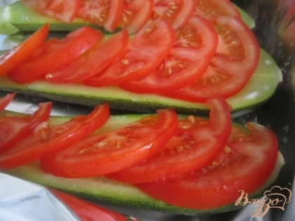 Готовые половинки цукини выложить на протвень . Немного посолить и разложить кусочки томатов.