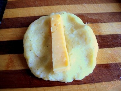 Добавить 1 яйцо, муку и крахмал, соль и перец по вкусу, хорошо перемешать. Сыр нарезать брусочками. Оставшееся яйцо взбить с солью. Из  картофельной массы сформировать мокрыми руками небольшие лепешки, положить по центру сыр.