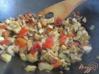 В сковроде на оливковом масле обжарить кубики томата и репчатый лук, затем добавить нарезанные мелко грибы. Накрыть крышкой и оставить потушиться минут 5-8.